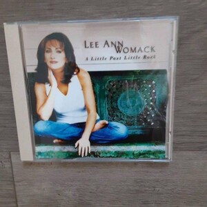 May include: A Lee Ann Womack music CD titled A Little Past Little Rock. The cover features a person with brown hair wearing a white sleeveless top and blue jeans, sitting cross-legged in front of a dark green, ornate, circular metal background.