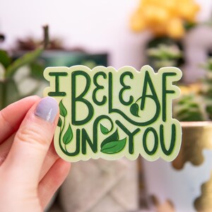 May include: A green and white sticker with the text "I beleaf in you" with green leaf illustrations.