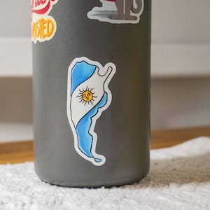 May include: A gray water bottle with a sticker of the outline of Argentina with the Argentinian flag inside. The flag is blue and white with a yellow sun in the center.