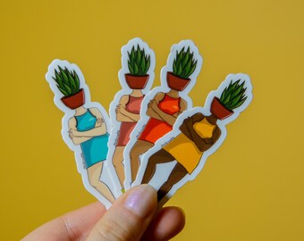 Puede incluir: Cuatro pegatinas coloridas que representan a una persona con una planta en maceta como cabeza. Cada pegatina tiene un vestido de un color diferente y una planta de un color diferente. Las pegatinas se sostienen en una mano.