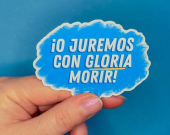 Puede incluir: Una pegatina azul con texto blanco que dice "¡O JUREMOS CON GLORIA MORIR!" en español. La pegatina tiene un borde en forma de nube y se sostiene sobre un fondo azul.