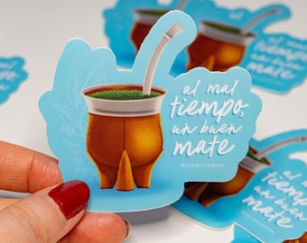Puede incluir: Una pegatina azul y blanca con una ilustración de dibujos animados de una calabaza mate tradicional con una pajita. El texto en la pegatina dice "al mal tiempo, un buen mate" y "@nicolcreates".