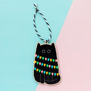 May include: Black cat Christmas ornament with colorful lights wrapped around it. The ornament is made of wood and has a string for hanging.