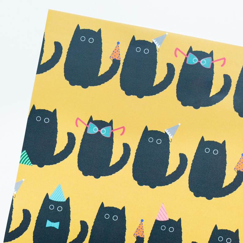 May include: A yellow wrapping paper with a repeating pattern of black cats wearing party hats and glasses. Some cats are wearing bow ties.