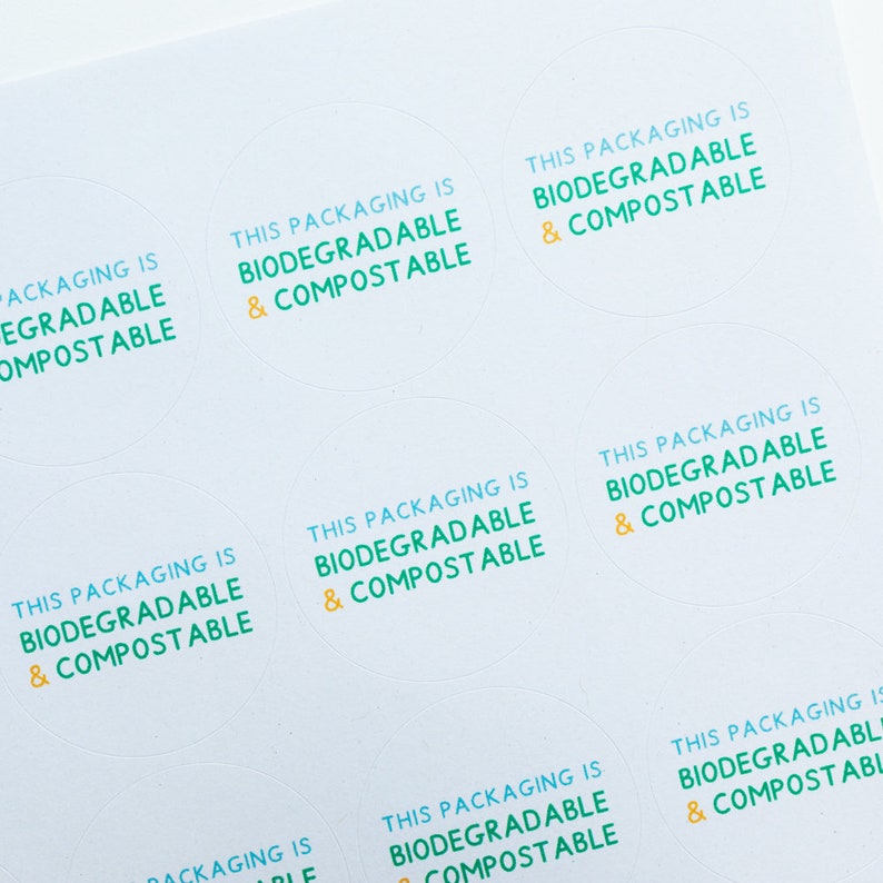 May include: A sheet of white paper with multiple round stickers that say "This packaging is biodegradable & compostable" in green and yellow text.