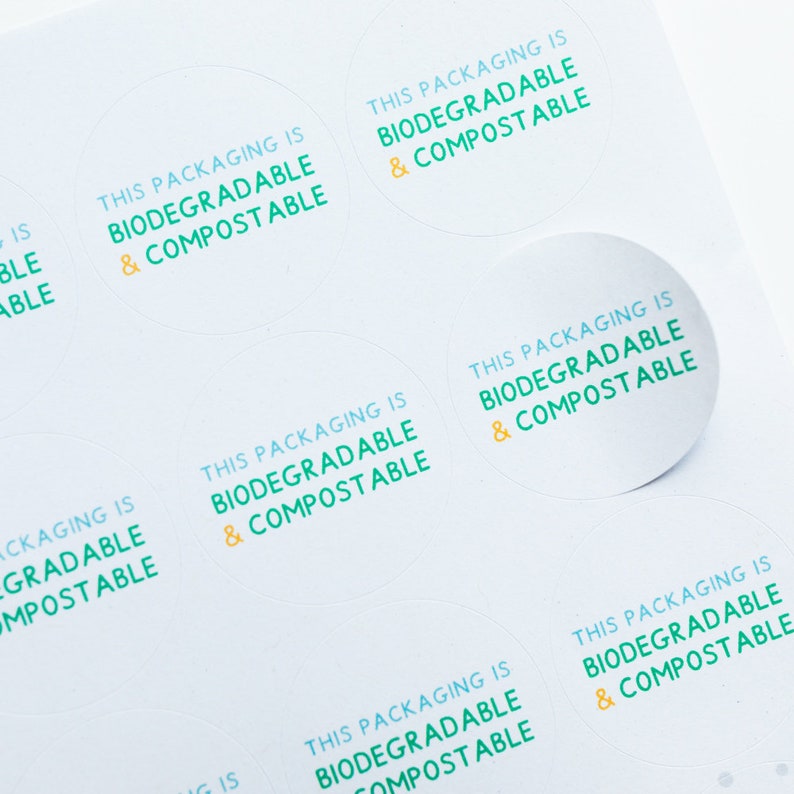 May include: A sheet of white paper with multiple round stickers. Each sticker has the text "This packaging is biodegradable & compostable" in blue and yellow text.