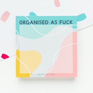 May include: Square notepad with the text "ORGANISED AS FUCK" in teal. The notepad has a light grey background with abstract shapes in yellow, pink, and teal, and white wavy lines. The bottom right corner has the text "JEFF AND THE SQUIRREL".