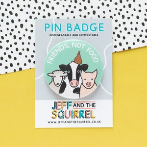 Può includere: Un badge verde e bianco con una mucca, un maiale, una pecora e un pollo. Il testo sul badge recita "Friends, Not Food". Il badge è su una carta bianca con il testo "Pin Badge, Biodegradable and Compostable, Jeff and the Squirrel, www.jeffandthesquirrel.co.uk".