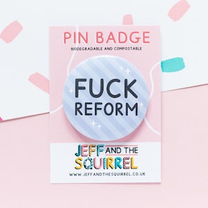 May include: A circular pin badge with the words "FUCK REFORM" in black on a light blue background with white diagonal stripes and star accents. The pin is on a pink card with the text "PIN BADGE" and "JEFF AND THE SQUIRREL" in colorful letters.