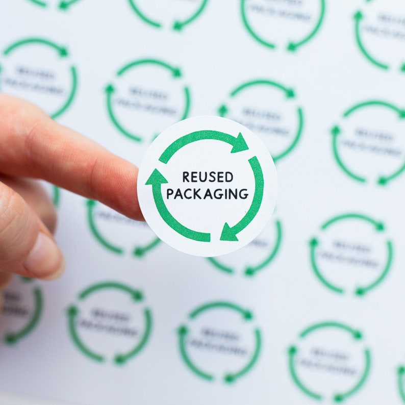May include: A white round sticker with a green recycling symbol and the text "REUSED PACKAGING" in black.