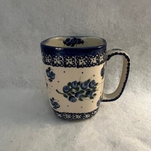May include: A white ceramic mug with a blue and white floral design. The mug has a square shape and a handle.