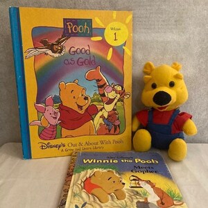 Könnte beinhalten: Ein Set aus zwei Winnie Puuh Kinderbüchern. Das erste Buch ist gelb mit dem Titel "Pooh Good as Gold" und zeigt Winnie Puuh und Ferkel. Das zweite Buch ist hellbraun mit dem Titel "Winnie Puuh trifft Gopher" und zeigt Winnie Puuh und Gopher. Ein gelbes Plüsch-Winnie Puuh-Spielzeug befindet sich im Vordergrund.