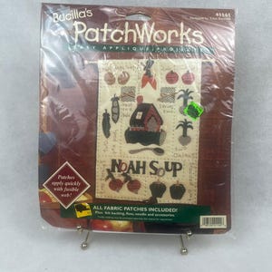 May include: A Bucilla's PatchWorks easy applique project kit. The kit includes fabric patches, felt backing, floss, needle, and accessories. The design features a house, vegetables, and the words "NOAH SOUP".
