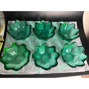 May include: Six emerald green glass bowls with a unique, scalloped petal design. The bowls are arranged in two rows of three, showcasing their vibrant color and elegant shape. These decorative bowls are ideal for serving snacks or displaying small items.