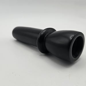 May include: A black, cylindrical smoking pipe with a rounded mouthpiece and a flared bowl. The pipe is made of a smooth, solid material and is set against a white background. The design is simple and elegant.