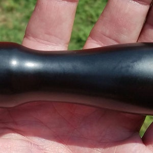 May include: A black, smooth, cylindrical handle with a slightly rounded end. The handle is made of a hard, durable material.