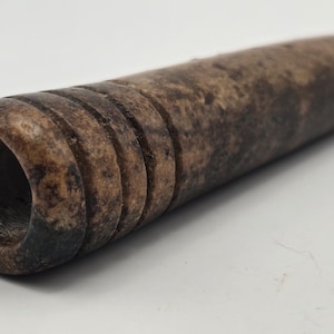 May include: A brown and black stone pipe with a smooth, rounded surface and a small hole at one end.