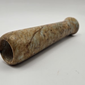 May include: A smooth, light brown and green stone pipe with a rounded end. The pipe is made of a marbled stone with a natural, organic look.