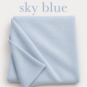 May include: A folded sky blue textile with a smooth surface on one side and a fine knit texture on the other. The text sky blue is printed in light blue letters above the fabric, which is a solid, light, cool-toned blue color.