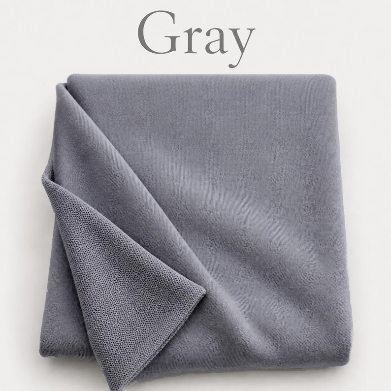 May include: A folded piece of gray fabric with a smooth, matte surface on the top layer and a visible textured, looped knit construction on the underside. The word Gray is printed in a simple serif font above the fabric.