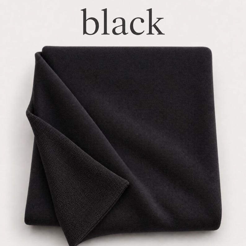 May include: A folded piece of solid black fabric with a visible knit texture. The word black is printed in a serif font above the textile. The fabric is square-shaped and displays a consistent dark tone throughout its surface area.