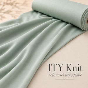 May include: A roll of sage green ITY knit fabric with a smooth, matte texture. The material is draped to show its fluid, soft stretch jersey quality. The text ITY Knit Soft stretch jersey fabric is printed in black on the lower right side.
