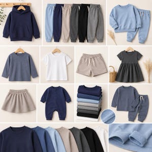 May include: A collection of children's clothing including a navy hoodie, various colored sweatpants, a light blue sweatshirt set, a long-sleeve shirt with a pocket, a white t-shirt, beige shorts, a dark dress, a skirt, a navy romper, and folded shirts.