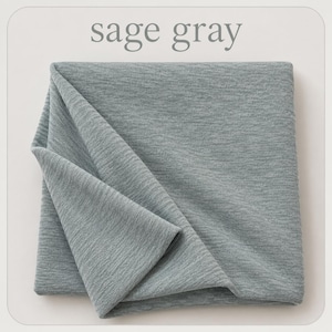 May include: A folded piece of sage gray fabric with a fine, textured knit surface. The material displays a soft, heathered appearance with subtle horizontal lines throughout the weave. The text sage gray is printed above the fabric.