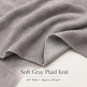 May include: A soft gray knit fabric featuring a plaid pattern with a textured surface. The fabric is 60 inches wide and weighs approximately 215 grams per square meter. The text Soft Gray Plaid Knit is printed on the image with the dimensions.