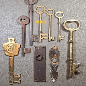 May include: A collection of vintage keys and door fittings. The keys are crafted from brass and iron, showcasing intricate designs. Includes a key with the number 21 and the word "Stephen" on it.