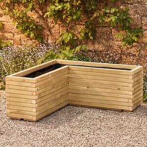 May include: A wooden corner planter with a black liner. The planter is made of natural wood and has a slatted design. It is sitting on a gravel surface.