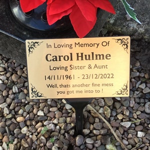 May include: Gold memorial plaque with black lettering on a grave. The plaque reads "In Loving Memory Of Carol Hulme Loving Sister & Aunt 14/11/1961 - 23/12/2022 Well, thats another fine mess you got me into to!"