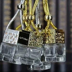 May include: Five glass car air fresheners with gold and silver metal caps and decorative designs. Each air freshener is attached to a gold or silver string.