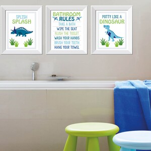 May include: Three framed prints with dinosaur illustrations and text. The prints say "Splish Splash", "Bathroom Rules", and "Potty Like a Dinosaur". The color scheme is blue, green, and white. The scene includes a bathtub, stools, and a blue towel.