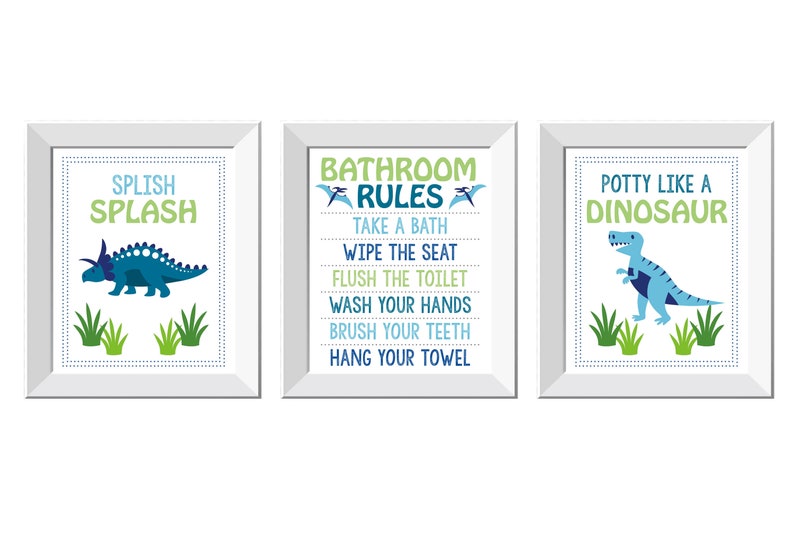 May include: Three framed prints with dinosaur-themed bathroom decor. The prints feature text like "Splish Splash," "Bathroom Rules," and "Potty Like a Dinosaur," along with dinosaur illustrations in blue and green. The frames are white.