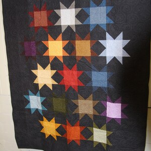 May include: A black quilt with a repeating pattern of colourful stars. The stars are arranged in a grid pattern and are made of different fabrics. The quilt is hanging on a wall.