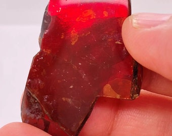 May include: A large, irregularly shaped piece of red amber with a smooth, polished surface. The amber is translucent and has a warm, reddish-brown hue.