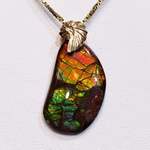 May include: A gold chain necklace with a pendant featuring a large, iridescent, multi-colored gemstone with a gold shell-shaped bail.