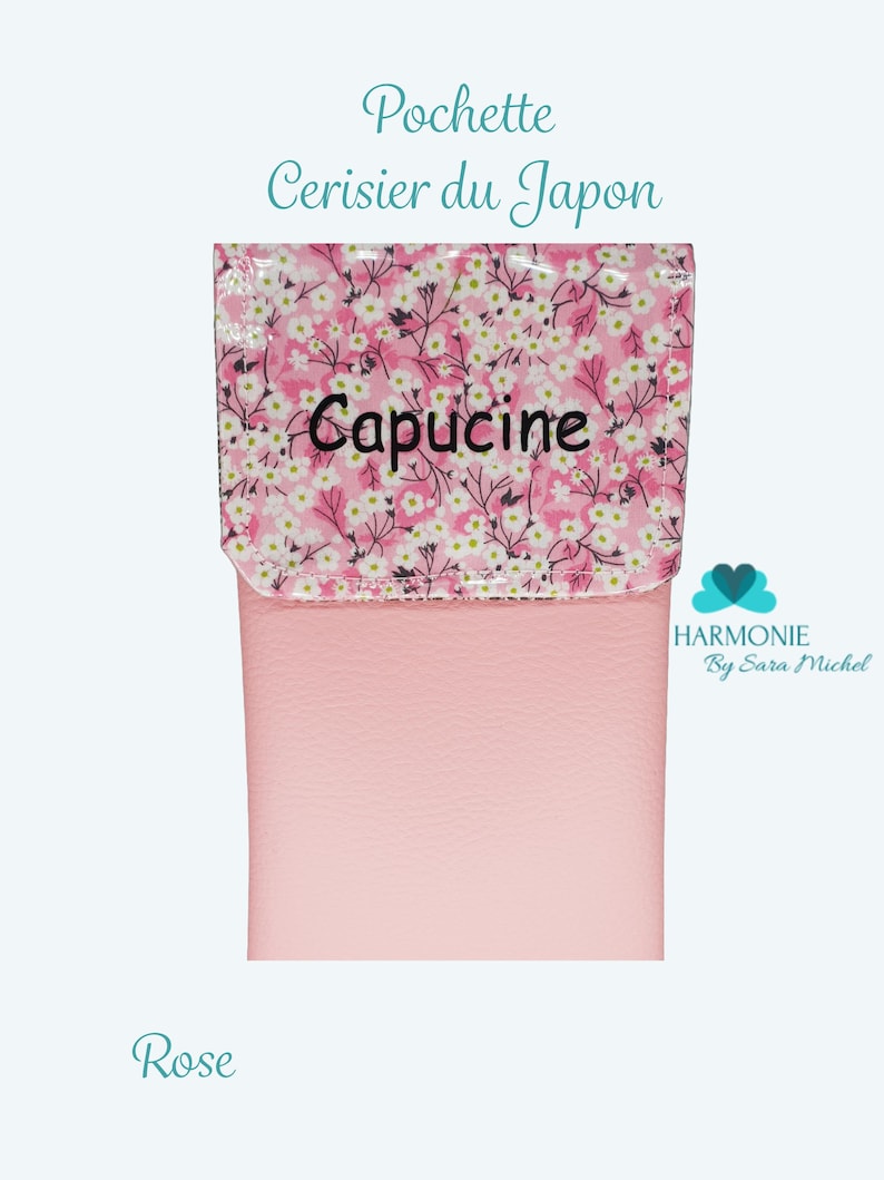 Puede incluir: Una bolsa rosa con una solapa estampada con flores blancas sobre un fondo rosa. La solapa tiene la palabra "Capucine" bordada en negro. El texto "Pochette Cerisier du Japon" est&aacute; encima de la solapa, y "Rose" en la parte inferior.