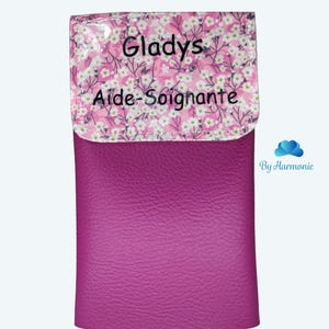 Puede incluir: Un estuche de color magenta con una solapa estampada con flores. La solapa presenta un fondo rosa con flores blancas y el nombre "Gladys" y las palabras "Aide-Soignante" impresas en negro. La parte inferior del estuche es de color magenta liso.