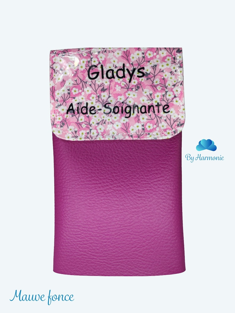Puede incluir: Un estuche de color magenta con una solapa estampada con flores. La solapa presenta un fondo rosa con flores blancas y el nombre "Gladys" y las palabras "Aide-Soignante" impresas en negro. La parte inferior del estuche es de color magenta liso.