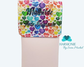 May include: A pink pouch with a rainbow heart pattern and the text "Mathilde Aide Soignante". The pouch is labeled "Pochette Pleine d'amour" and "Rose Clair". The brand name "Harmonie By Sara Michel" is also visible.