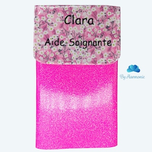 Puede incluir: Un estuche fucsia brillante con una solapa estampada floral. La solapa tiene el nombre "Clara" y las palabras "Aide-Soignante" impresas. La parte inferior del estuche tiene las palabras "Fuchsia paillette".