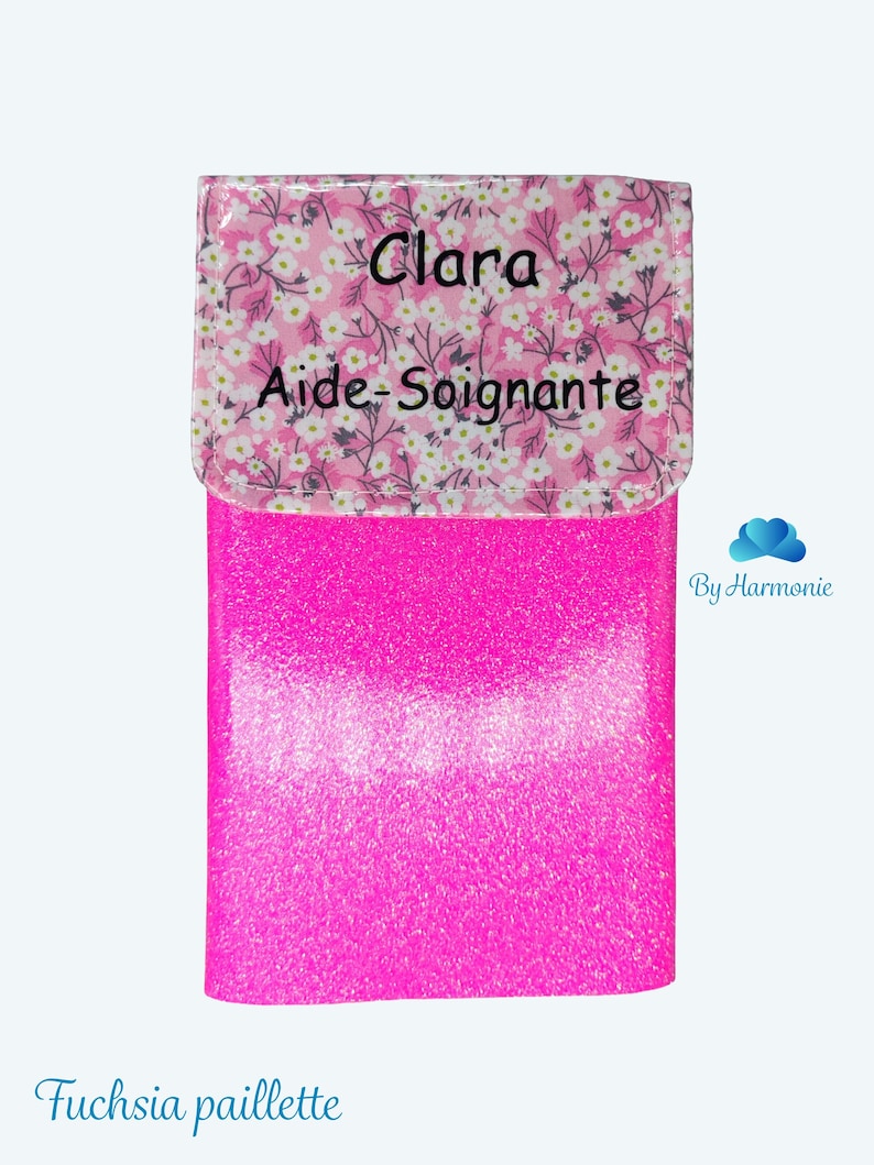 Puede incluir: Un estuche fucsia brillante con una solapa estampada floral. La solapa tiene el nombre "Clara" y las palabras "Aide-Soignante" impresas. La parte inferior del estuche tiene las palabras "Fuchsia paillette".
