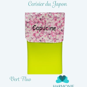 Puede incluir: Una peque&ntilde;a bolsa rectangular con una base verde ne&oacute;n brillante y una solapa estampada floralmente. La solapa presenta un fondo rosa con flores blancas y la palabra "Capucine" en negro. El texto en la bolsa dice "Pochette Cerisier du Japon" y "Vert Fluo".