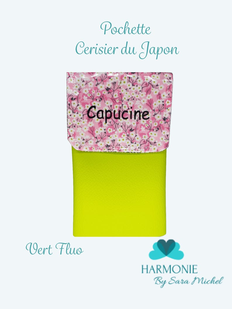 Puede incluir: Una peque&ntilde;a bolsa rectangular con una base verde ne&oacute;n brillante y una solapa estampada floralmente. La solapa presenta un fondo rosa con flores blancas y la palabra "Capucine" en negro. El texto en la bolsa dice "Pochette Cerisier du Japon" y "Vert Fluo".