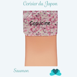 Puede incluir: Una bolsa de color salm&oacute;n con una solapa estampada floral. La solapa presenta un fondo rosa con flores blancas y la palabra "Capucine". El texto "Pochette Cerisier du Japon" est&aacute; encima de la bolsa.