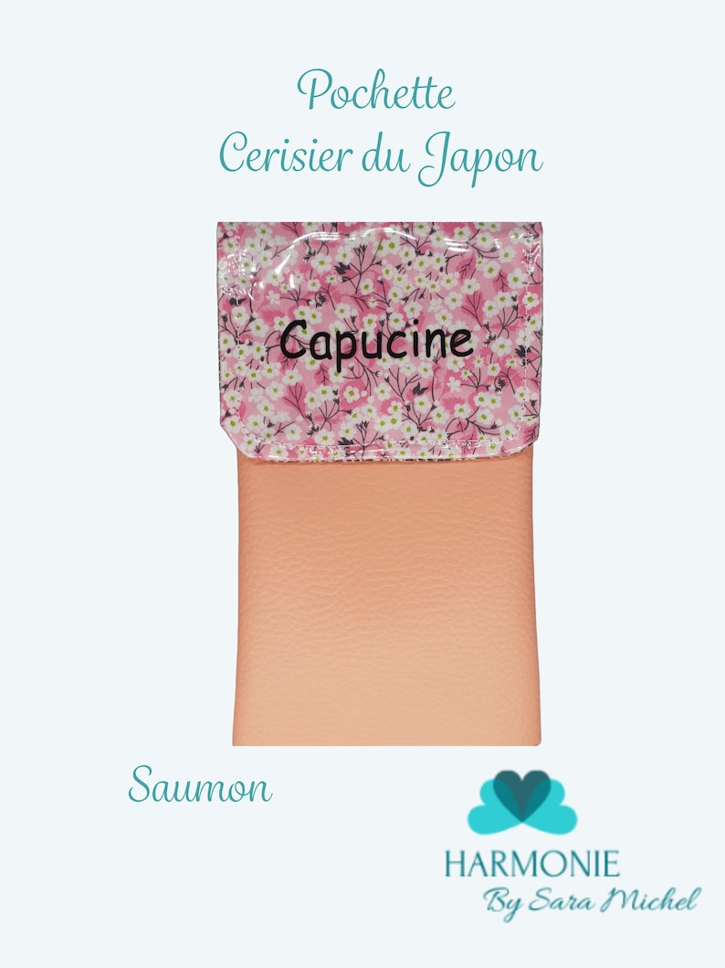 Puede incluir: Una bolsa de color salm&oacute;n con una solapa estampada floral. La solapa presenta un fondo rosa con flores blancas y la palabra "Capucine". El texto "Pochette Cerisier du Japon" est&aacute; encima de la bolsa.