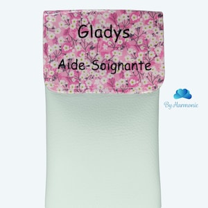 Puede incluir: Un estuche verde claro con una solapa estampada floral. La solapa presenta un fondo rosa con flores blancas y el nombre "Gladys" y las palabras "Aide-Soignante" en texto negro. La parte inferior del estuche tiene las palabras "Vert clair" en texto azul.