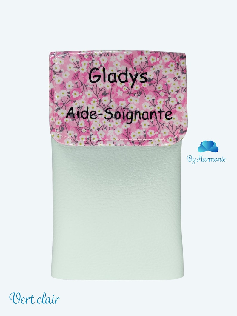 Puede incluir: Un estuche verde claro con una solapa estampada floral. La solapa presenta un fondo rosa con flores blancas y el nombre "Gladys" y las palabras "Aide-Soignante" en texto negro. La parte inferior del estuche tiene las palabras "Vert clair" en texto azul.